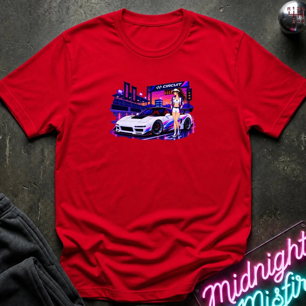 A red  short-sleeve t-shirt laid flat on a dark textured surface, featuring a colorful graphic print of a white sports car and a woman in a neon-lit scene. 