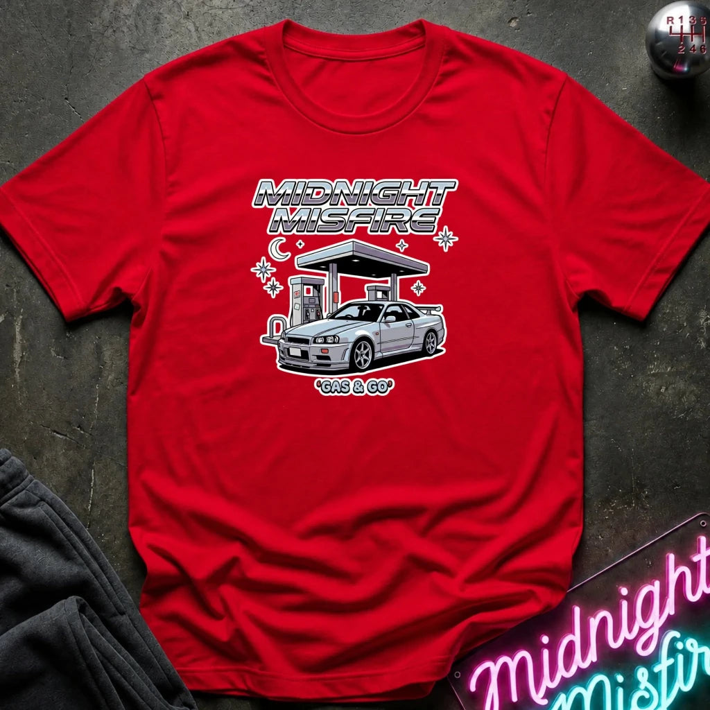 A red short-sleeve t-shirt with a graphic print of a silver Nissan S13 'Kits & Co' car at a gas station under the text 'MIDNIGHT MISFIRE' and 'gas & GO', laid flat on a dark textured surface.