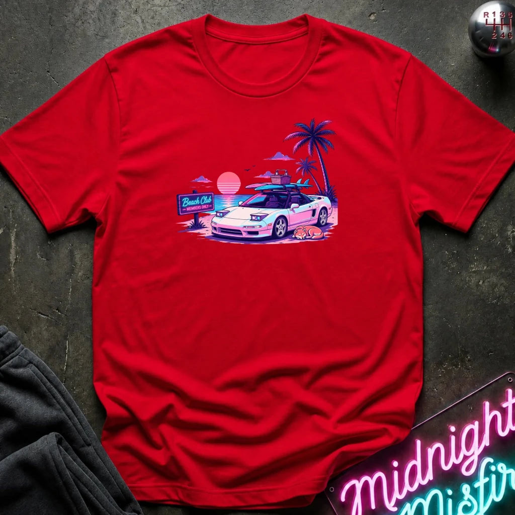 A red short-sleeve t-shirt laid flat on a dark textured surface, featuring a colorful retro graphic of a white sports car on a beach with palm trees and a sunset.