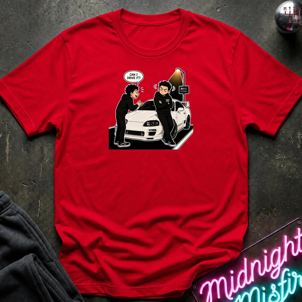 A red short-sleeve graphic t-shirt laid flat on a dark textured surface. The graphic shows two cartoon characters standing next to a white sports car, with one character saying 'CAN DRIVE IT' in a speech bubble.