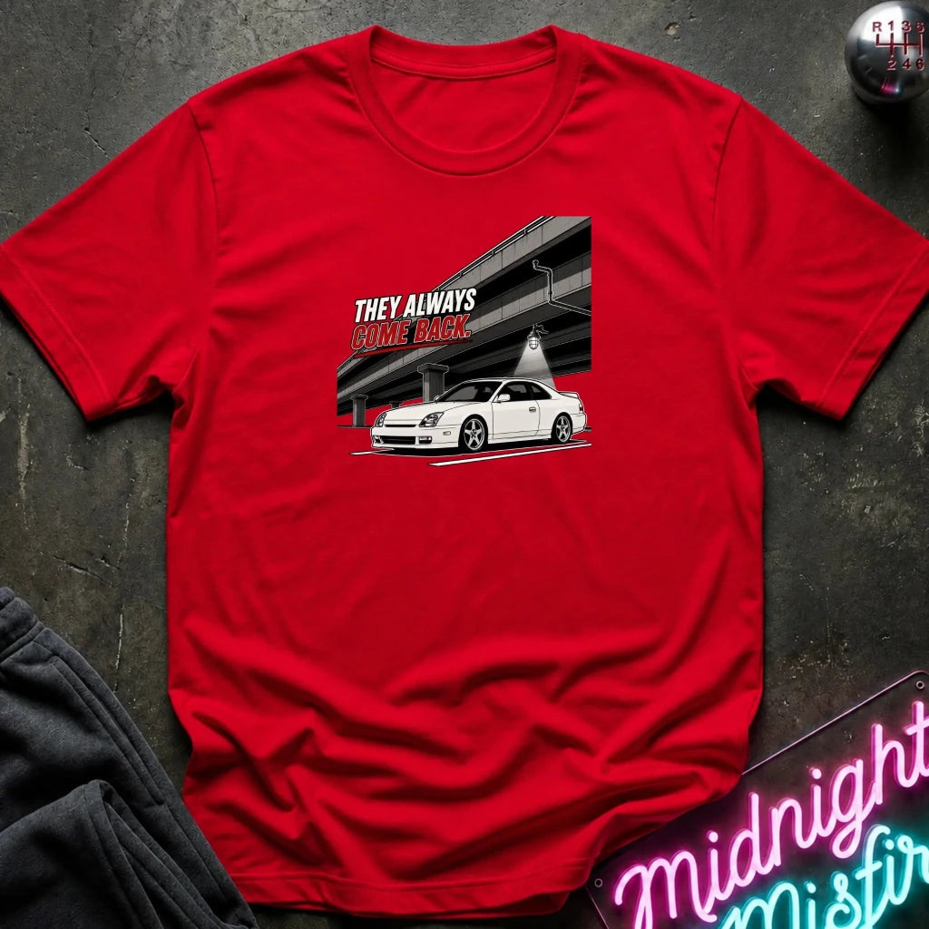 A red short-sleeve crewneck t-shirt laid flat on a dark textured surface. The shirt features a graphic print of a white sports car under an overpass 