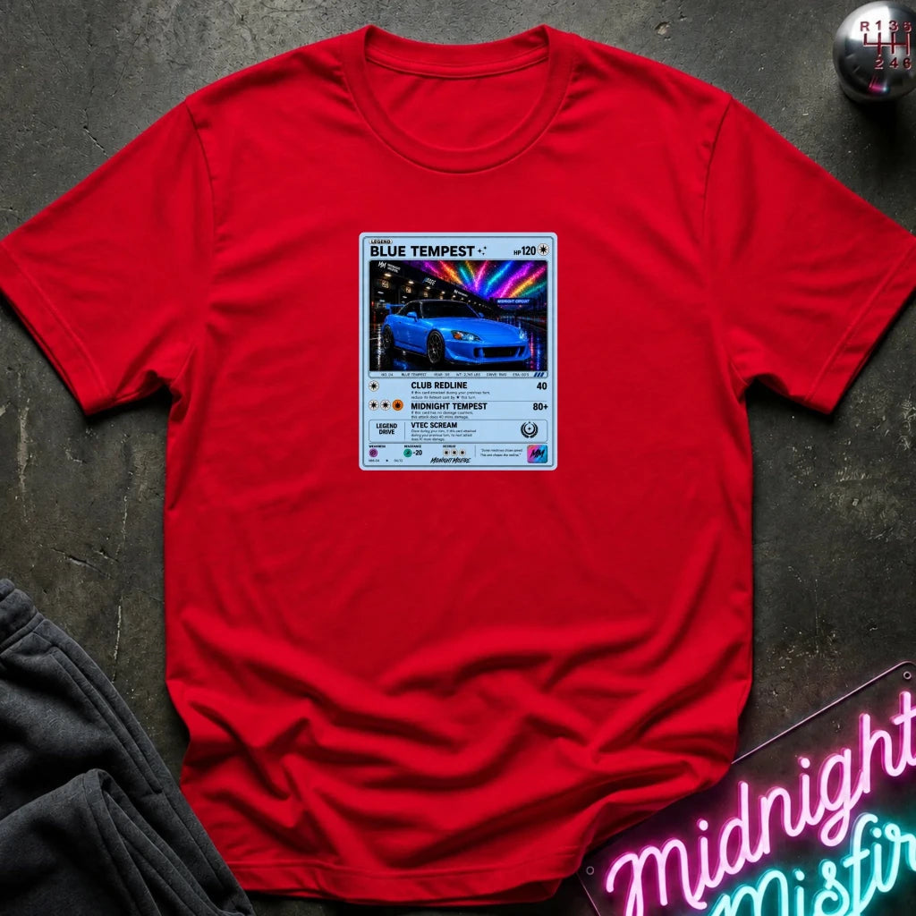 red crewneck t-shirt laid flat on a dark textured surface, featuring a graphic print of vintage card and a car.