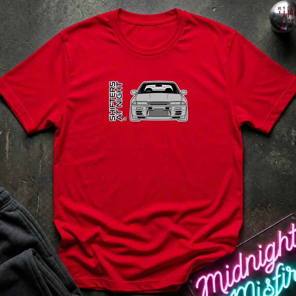 A red short-sleeve crewneck t-shirt laid flat on a dark textured surface, featuring a graphic of a gray sports car and the vertical text 'SHINERIGHT' on the chest.