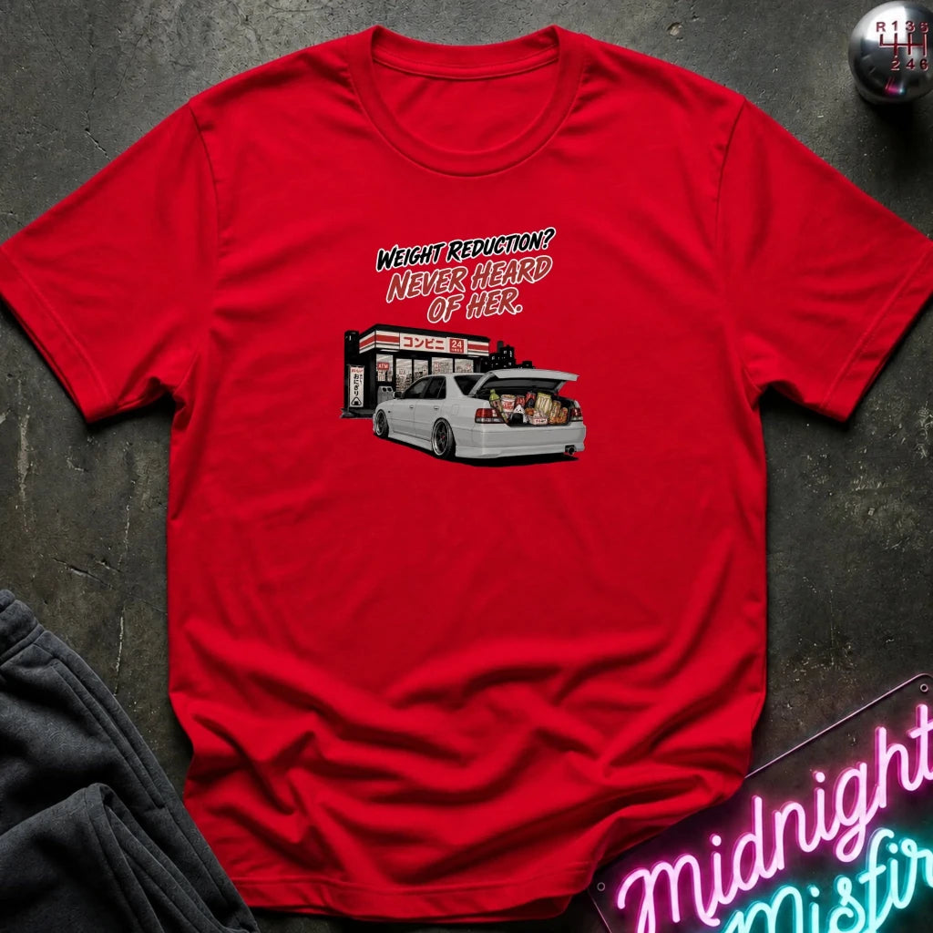 A red short-sleeve crewneck t-shirt with a graphic print of a white station wagon with its trunk open, next to a gas station counter, and the text 'WEIGHT REDUCTION? NEVER HEARD OF HER.' The shirt is laid flat on a dark textured surface with a gray sweatshirt and a neon sign partially visible.