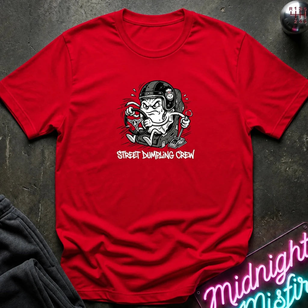 red crewneck t-shirt laid flat on a dark textured surface. The shirt features a graphic of a street-dumper character wearing a helmet and goggles, with the text 'STREET DUMPING CREW' printed below in a pink font.