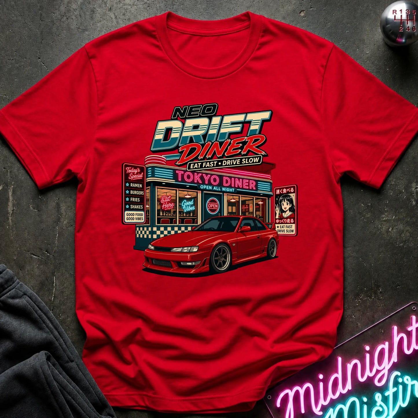 A red short-sleeve graphic T-shirt laid flat on a dark textured surface. The shirt features a colorful retro diner illustration with the text 'NEO DRIFT DINER' and 'TOKYO DINER,' plus a red sports car graphic.