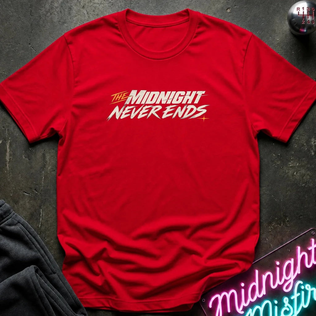 A red short-sleeve crewneck t-shirt with a stylized graphic reading 'THE MIDNIGHT NEVER ENDS' in white and yellow, laid flat on a dark textured surface with decorative props.