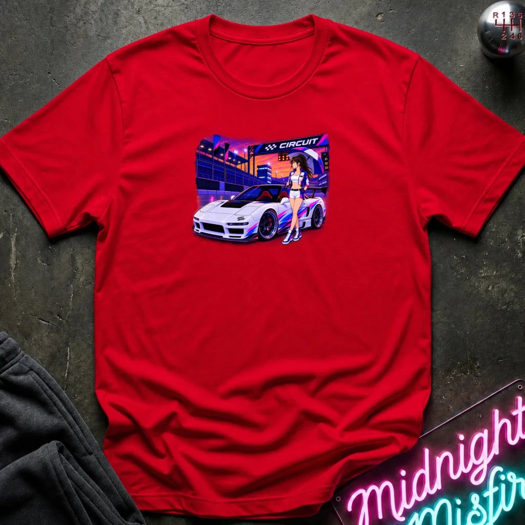 A bright red short-sleeve t-shirt laid flat on a dark textured surface, featuring a colorful graphic print of a white sports car and a woman in a neon-lit scene. 