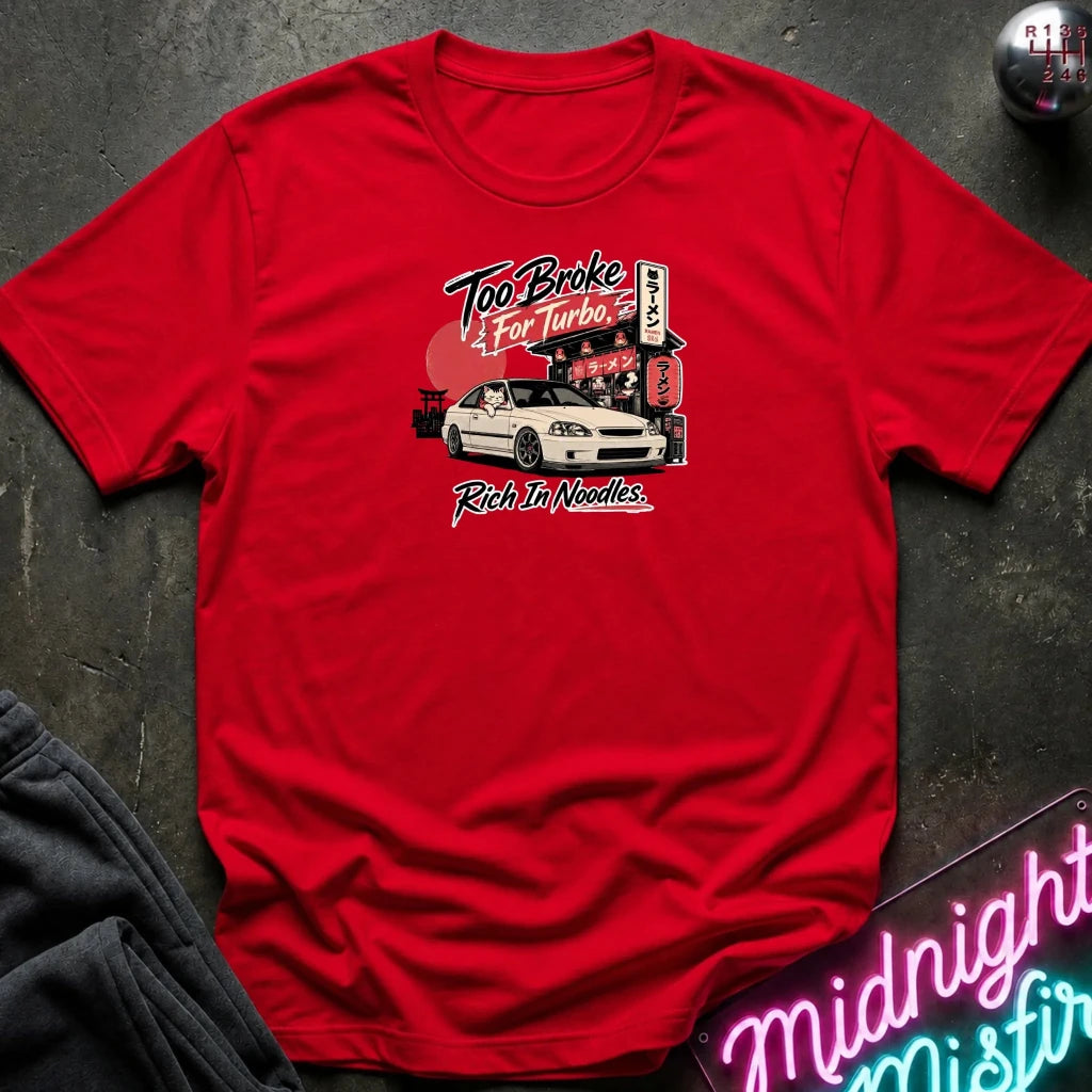 A red short-sleeve graphic T-shirt laid flat on a dark textured surface. The shirt features a central graphic of a white sports car with Japanese signage and the text 'Too Broke For Turbo' and 'Rich In Noodles.
