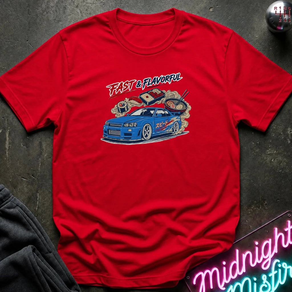 A red short-sleeve graphic T-shirt laid flat on a dark textured surface. The shirt features a colorful print of a blue sports car with ramen noodles and chopsticks, plus the text 'FAST & FLAVORFUL' in red and black.