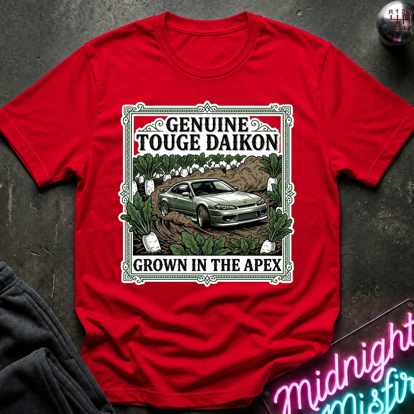 A red short-sleeve graphic T-shirt laid flat on a dark textured surface. The shirt features a large rectangular front print with the words 'GENUINE TOUGHE DAIKON' and 'GROWN IN THE APEX'.