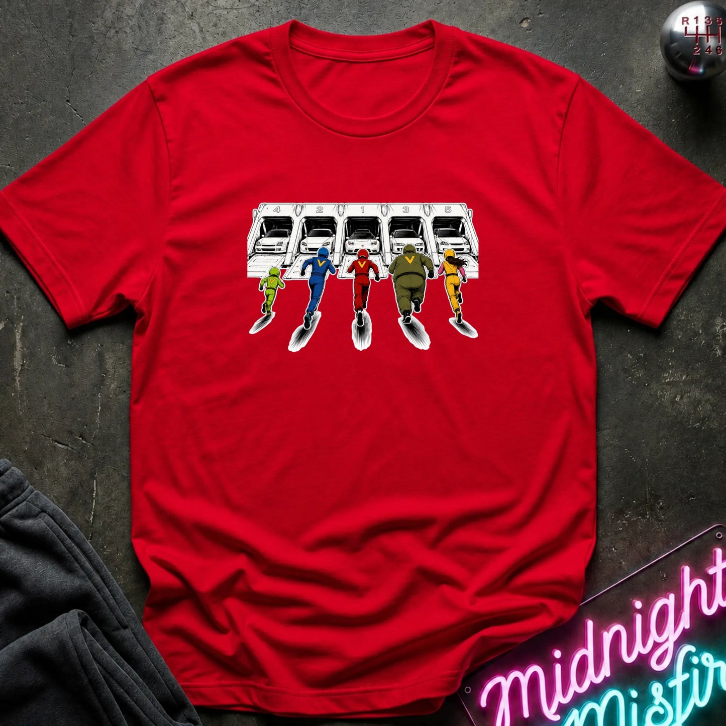 A red short-sleeve graphic T-shirt laid flat on a dark textured surface. The shirt features a printed illustration of a white sports cars in 5 different launch  pods.