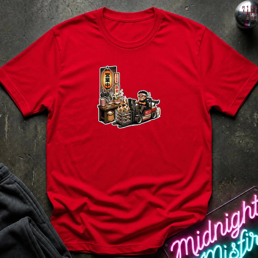 A red short-sleeve t-shirt with a cartoon graphic of a street food vendor on a forklift, laid flat on a dark textured surface with a neon sign and folded sweatpants nearby.