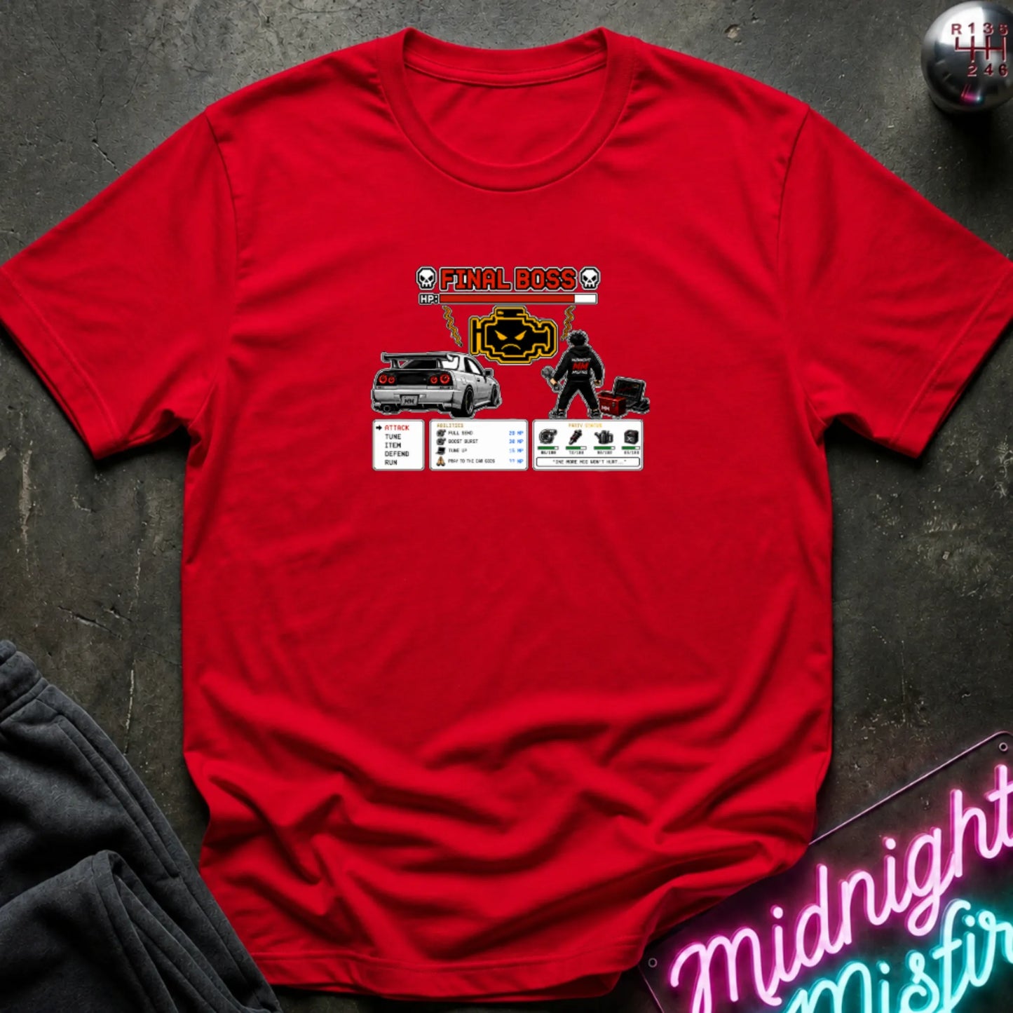 A red short-sleeve crewneck t-shirt laid flat on a dark textured surface, featuring a central graphic print of a rpg character and a car. 