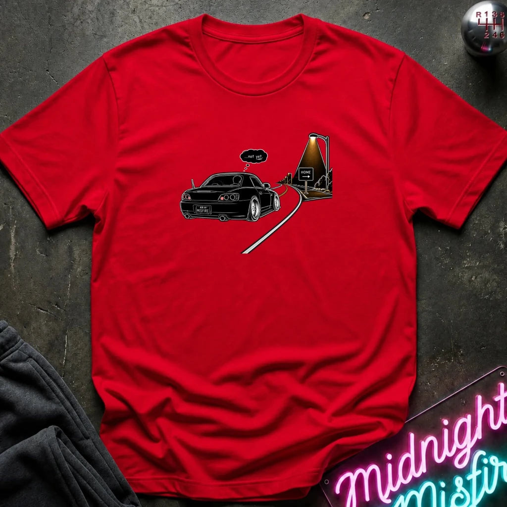A red short-sleeve t-shirt laid flat on a dark textured surface, featuring a graphic print of a black sports car driving passed sign that says home.