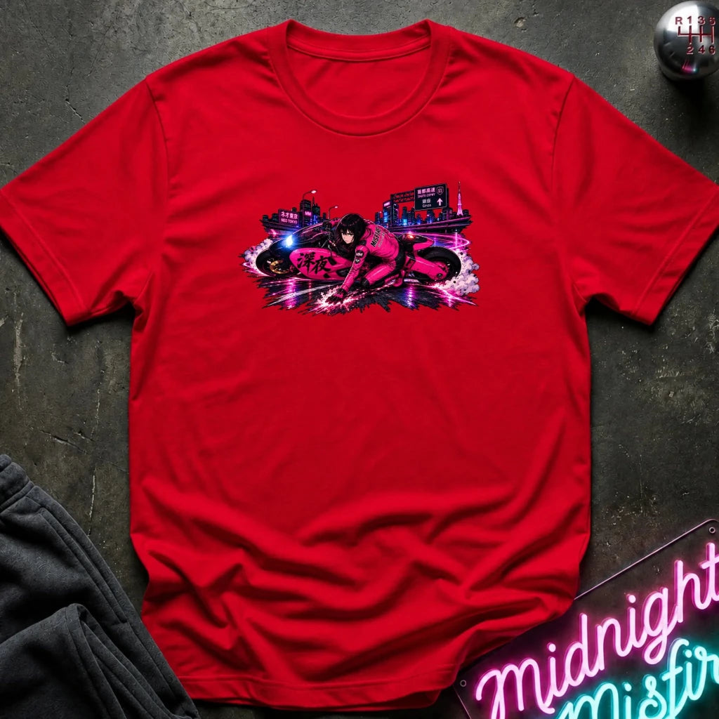 A red short-sleeve crewneck t-shirt with a colorful graphic print of a futuristic motorcycle racer on the chest, styled flat on a dark textured surface with a neon sign and dark pants partially visible.
