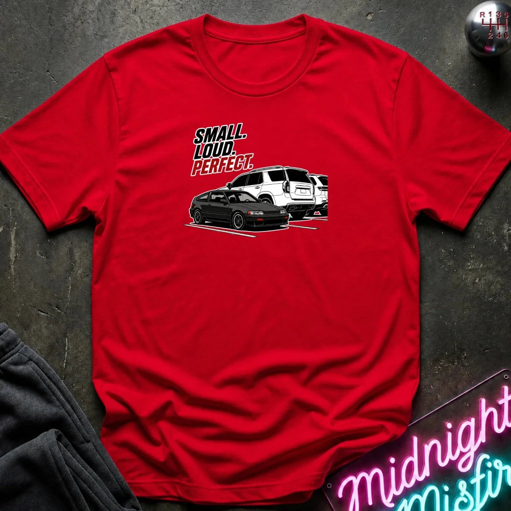 red  short-sleeve graphic t-shirt laid flat on a dark textured surface. The graphic features the text 'SMALL louD PERFECT.