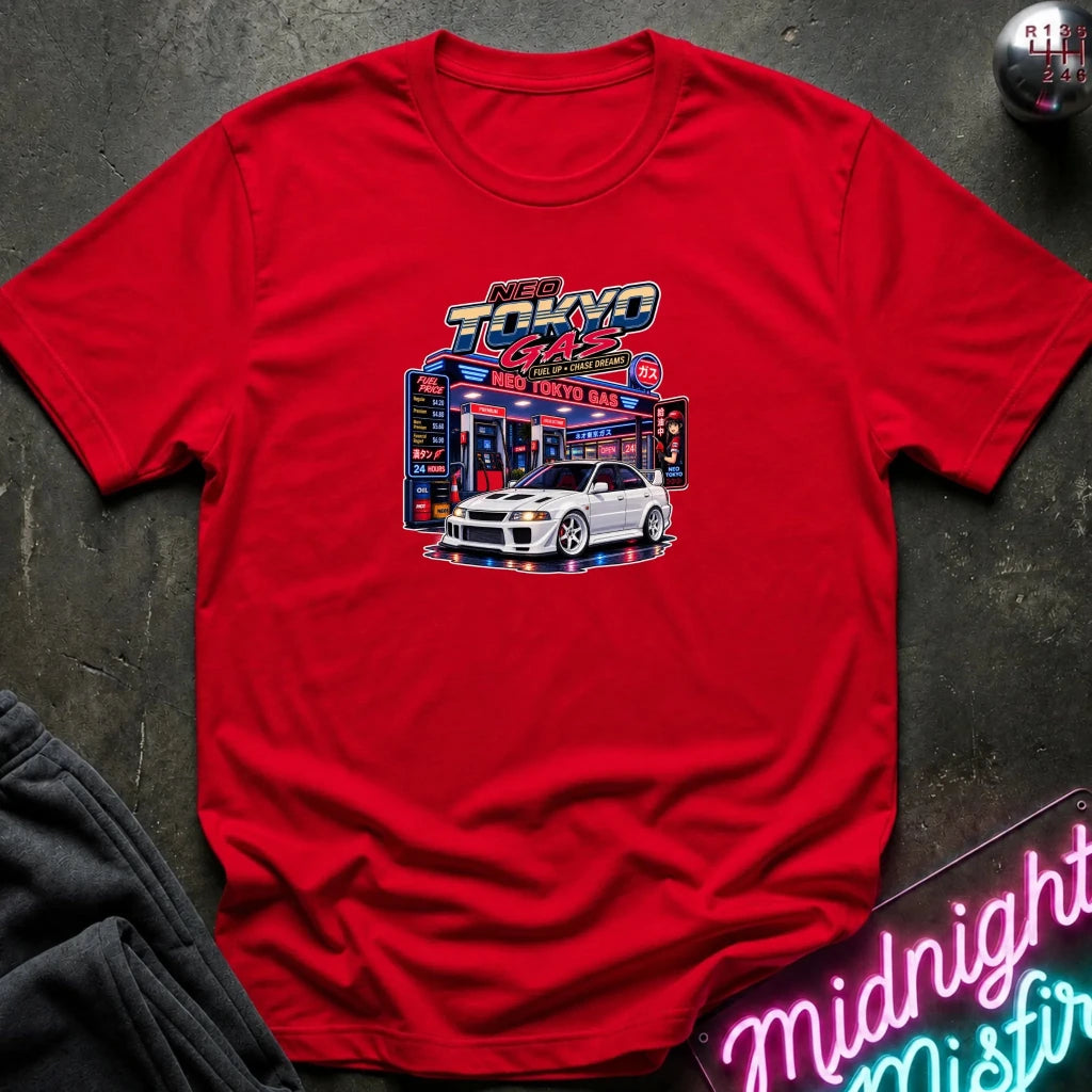 A red short-sleeve crewneck t-shirt featuring a 'Neo Tokyo Gas' graphic with a white sports car, laid flat on a dark textured surface with a neon sign and sweatpants as props.