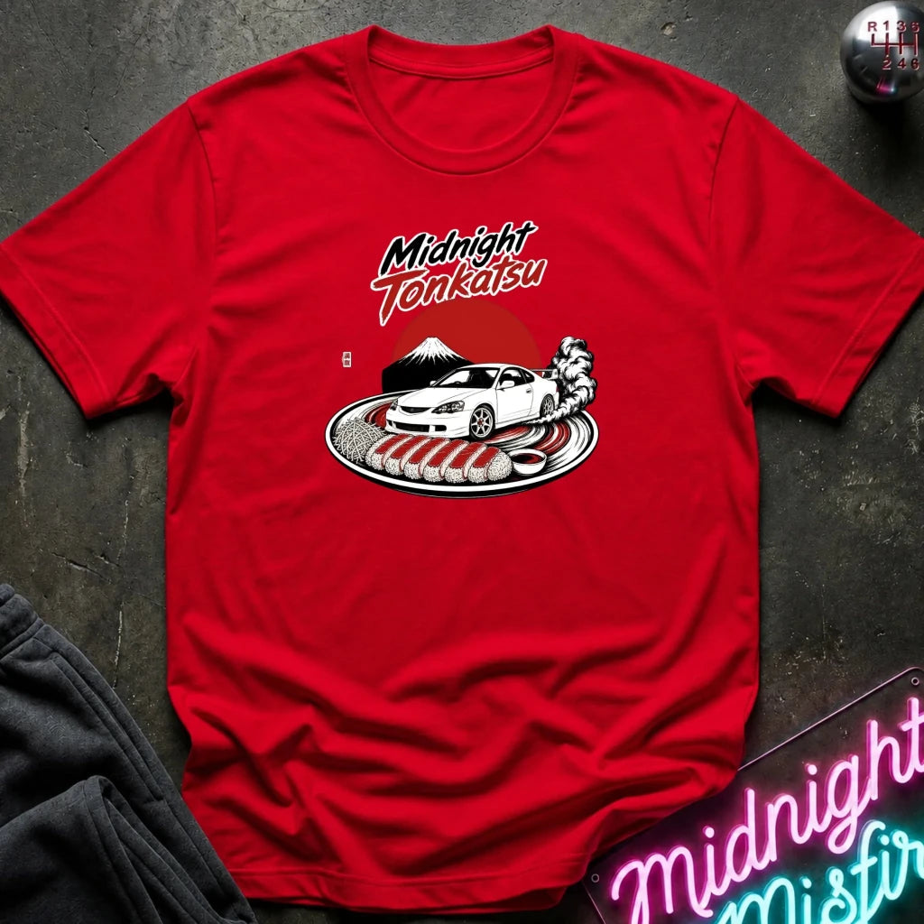 A red short-sleeve graphic T-shirt laid flat on a dark textured surface. The shirt features a printed design of a white sports car on a plate with red and the words 'Midnight Tonkatsu' in stylized lettering.