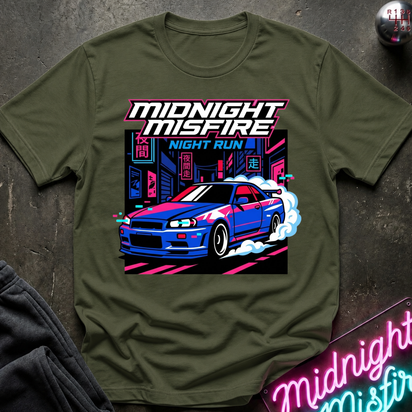 An olive green short-sleeve t-shirt with a vibrant graphic print of a blue and white sports car drifting in front of a neon-lit cityscape. The text 'MIDNIGHT MISFIRE' is written in a stylized white font with a pink outline above the car, and 'NIGHT RUN' appears below.