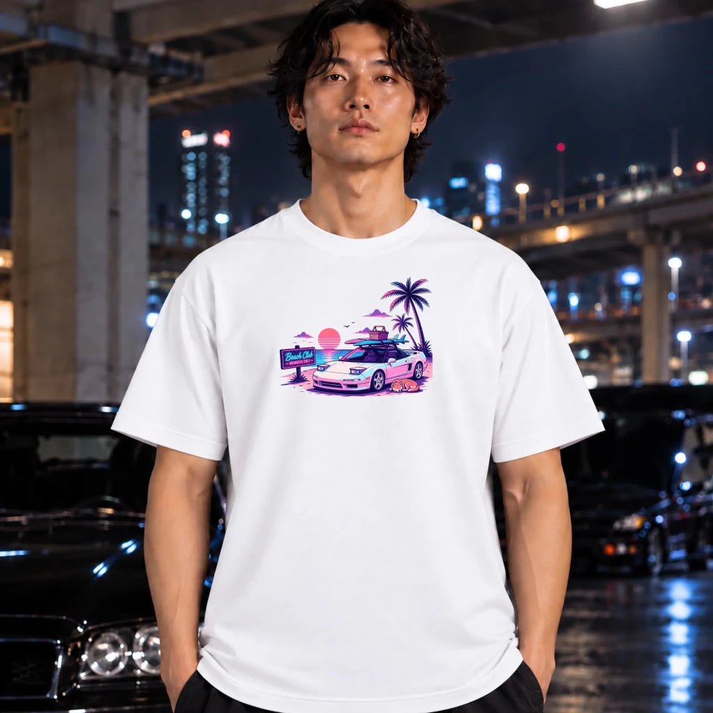 A man wearing a white crewneck t-shirt with a colorful graphic print of a car and palm trees, standing in front of a blurred night city background with cars.