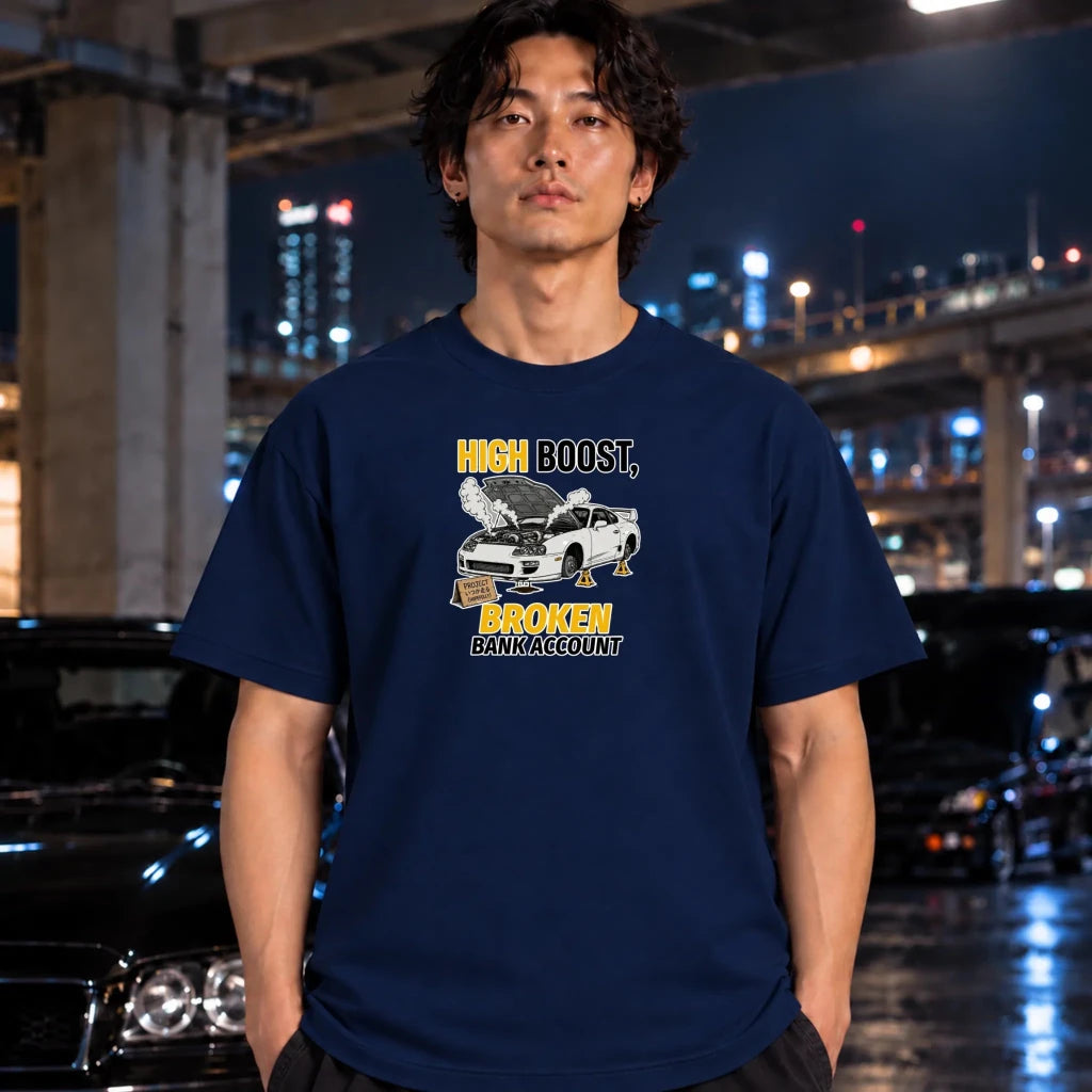 A man wearing a white crewneck t-shirt with a colorful graphic print of a car and palm trees, standing in front of a blurred night city background with cars.