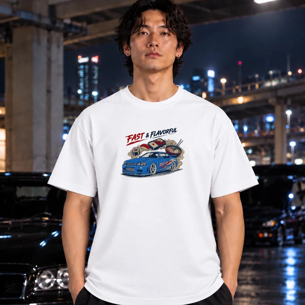 A man wearing a white graphic t-shirt with a blue car and 'FAST & FLAVORFUL' text, standing in a city environment at night with cars and lights in the background.