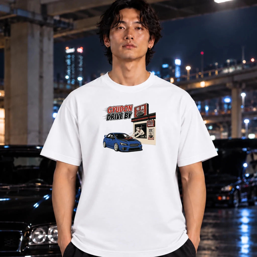 A man wearing a white graphic t-shirt with a 'Gyudon Drive By' car print, standing in front of a blurred night city background with cars.