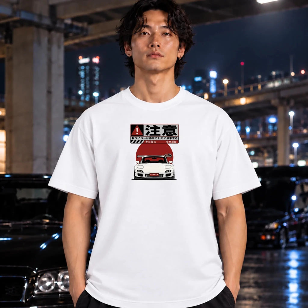 A man wearing a white graphic t-shirt with a white car illustration, standing in front of a blurred night city background with cars.