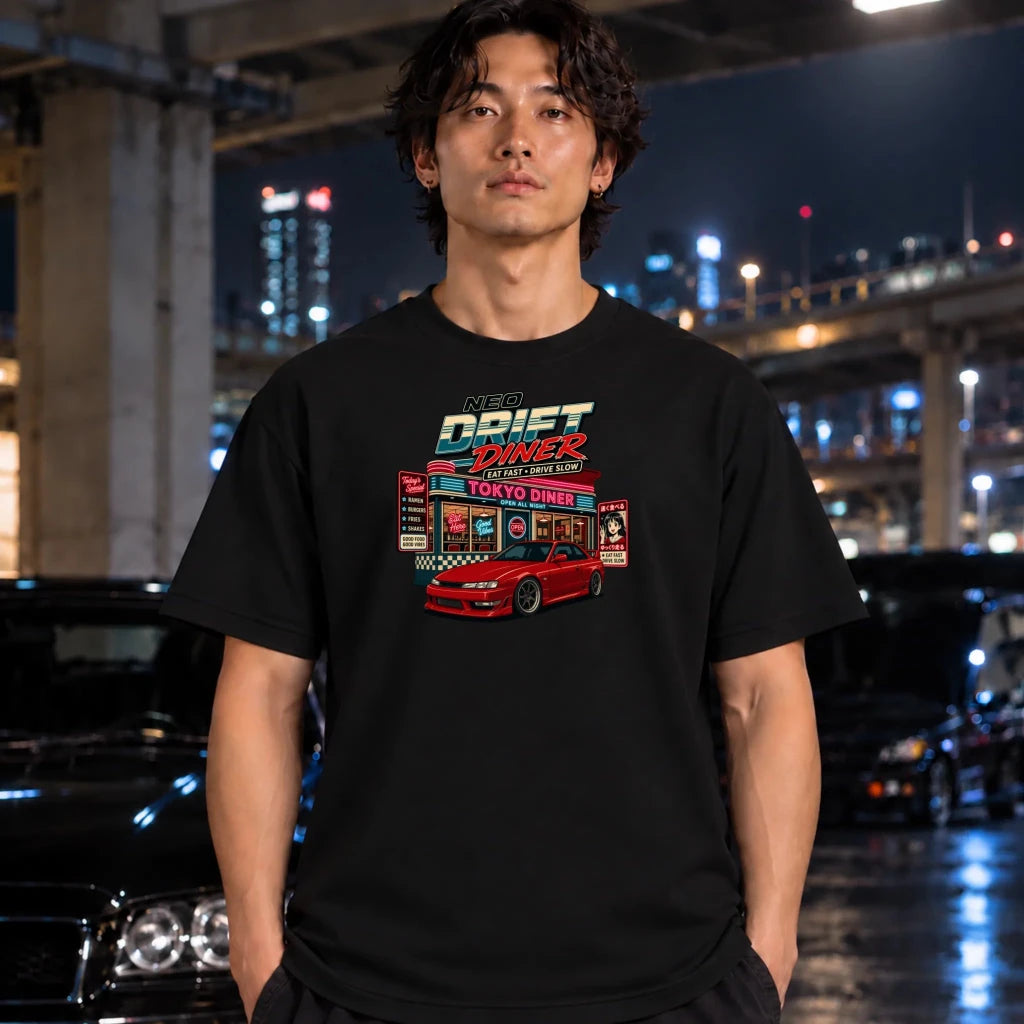 A man wearing a black graphic t-shirt with a 'Drift Diner Tokyo' design, standing in front of a blurred night cityscape with cars.
