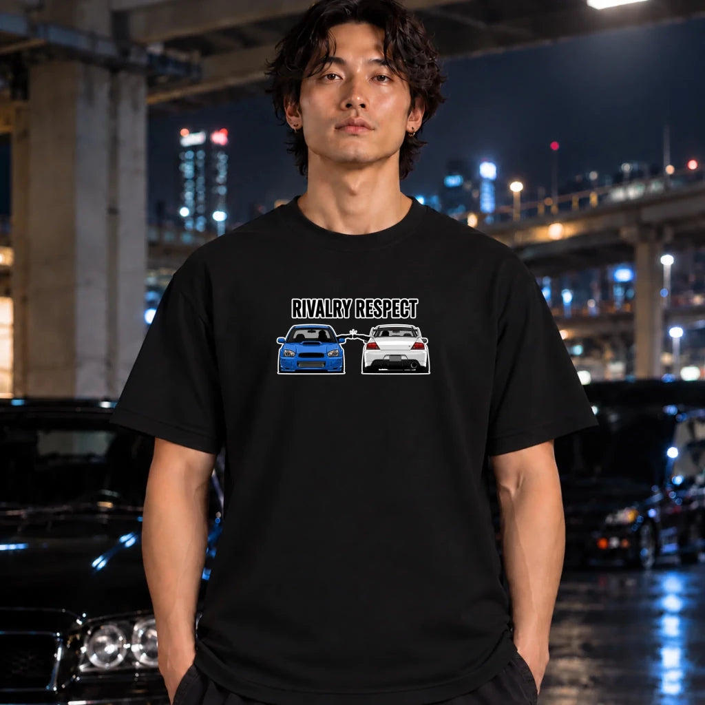 A man wearing a black graphic t-shirt with a 'RIVALRY RESPECT' design featuring two cars, standing in a city parking lot at night.