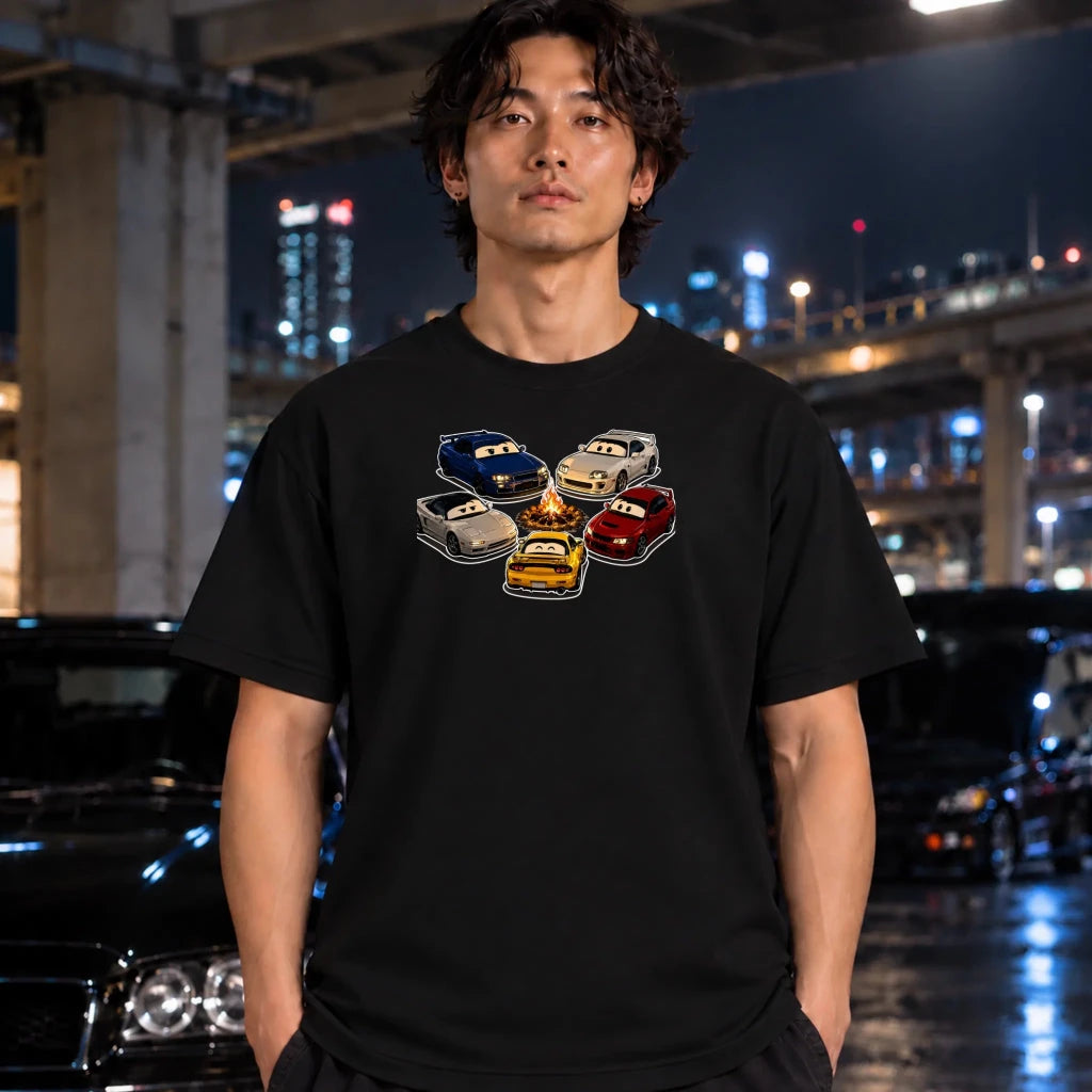 A man wearing a black t-shirt with a graphic of cartoon cars in various colors, standing in a city parking structure at night.