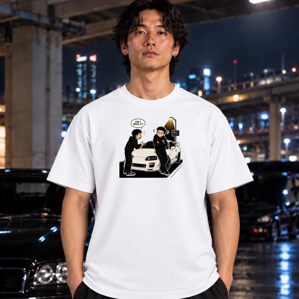 A man wearing a white graphic t-shirt with a black and white cartoon illustration of two characters standing next to a white car. The background is a blurred night city scene with lights and wet pavement.