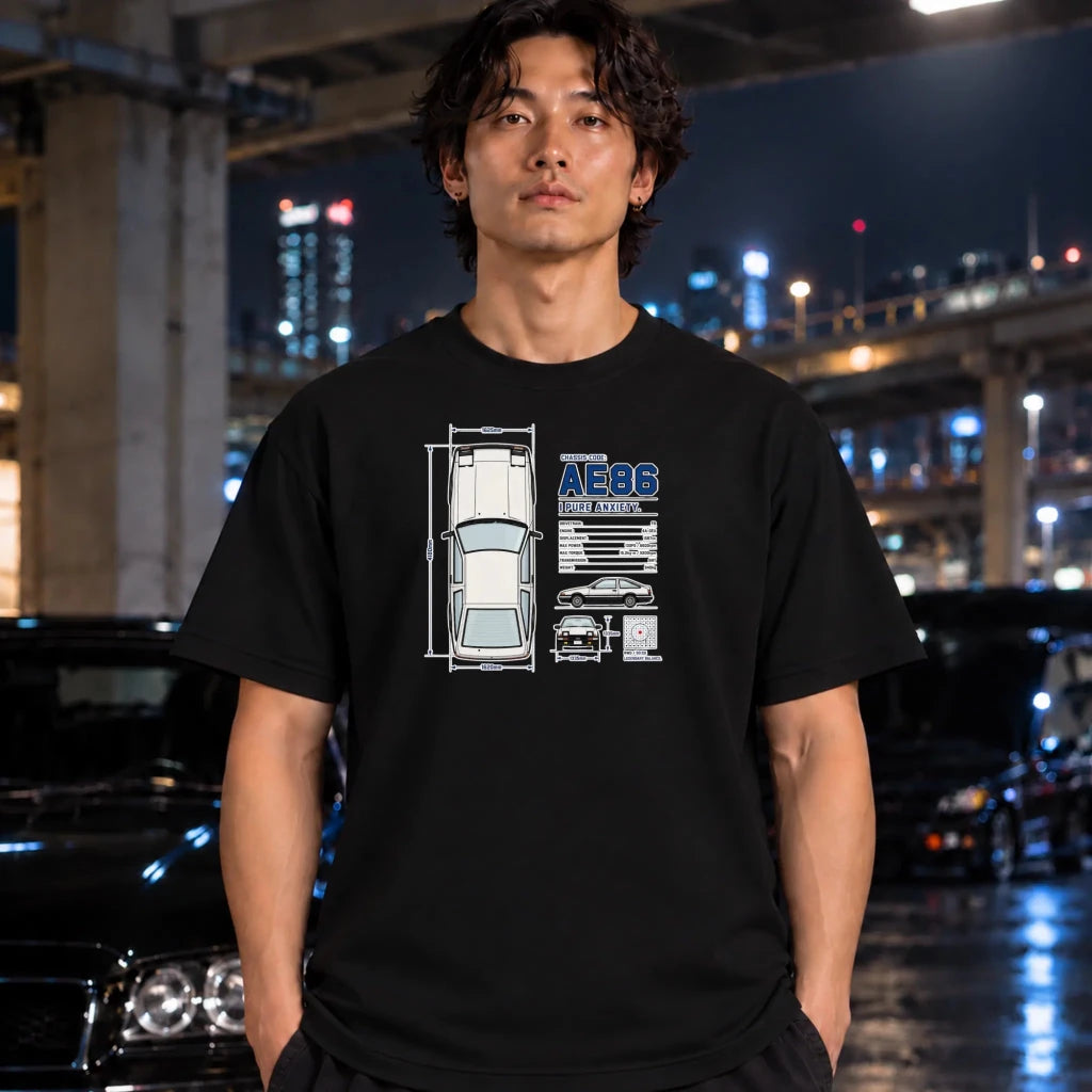 A man wearing a black graphic t-shirt with a car schematic and 'AEBS' text, standing in a nighttime urban setting with blurred cars and city lights in the background.