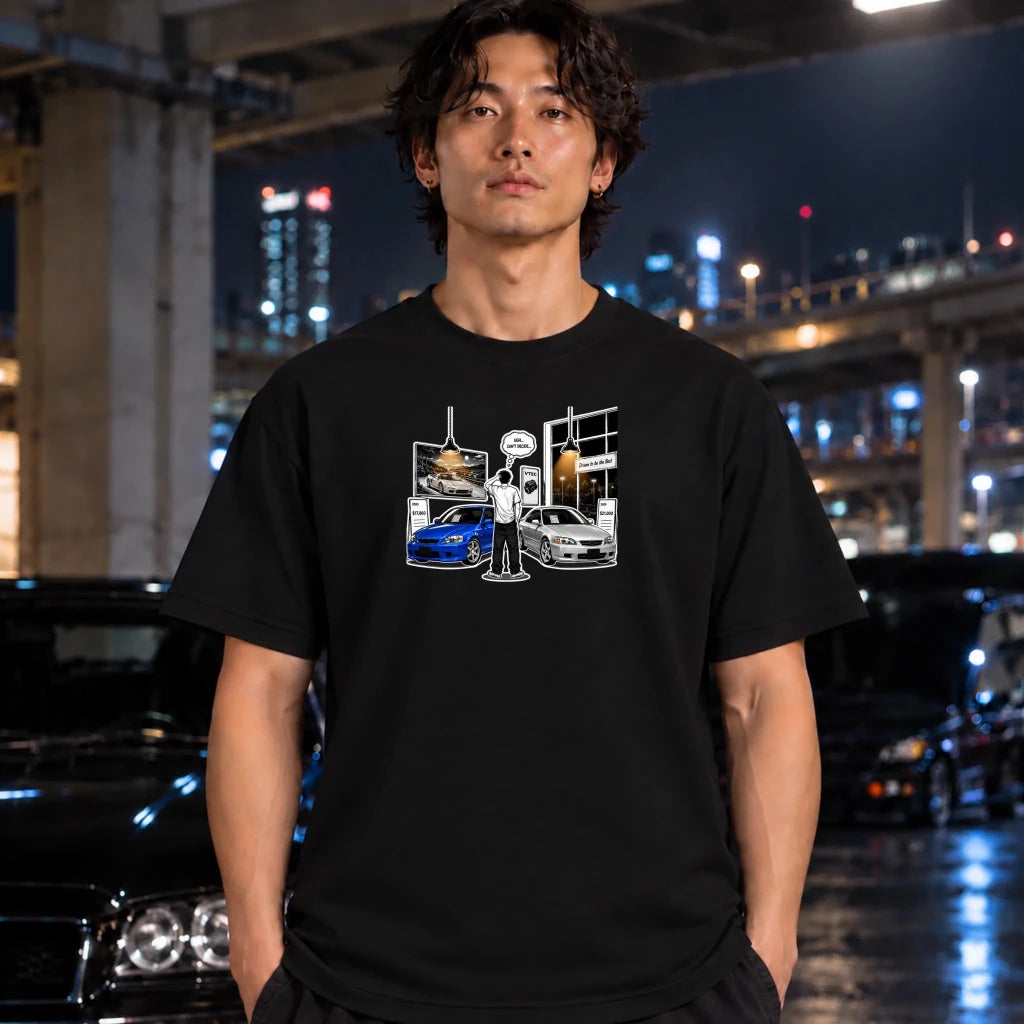 A man wearing a black graphic t-shirt with a white and blue car illustration, standing in a wet urban night scene with blurred cars and city lights in the background.