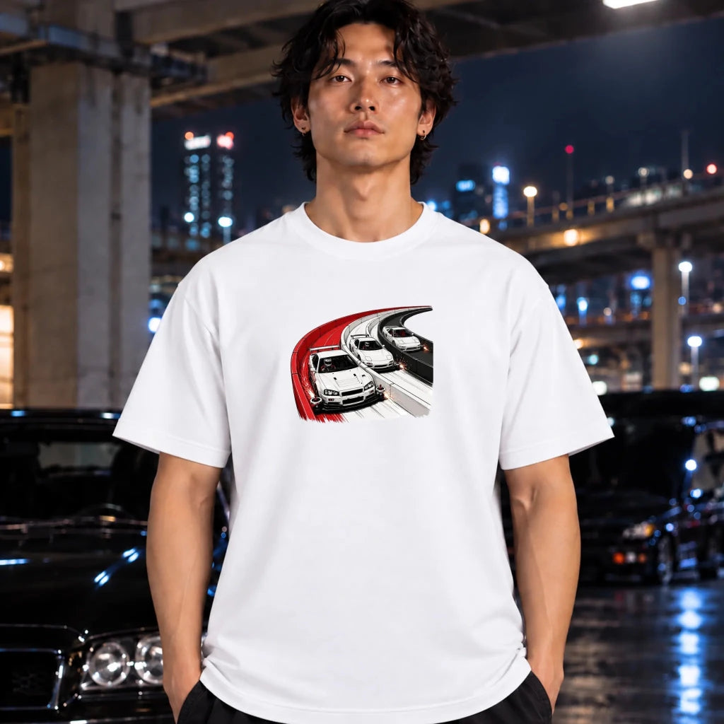 A man wearing a white short-sleeve t-shirt with a graphic print of a white sports car on a curved road, standing in front of a blurred night city background with cars.