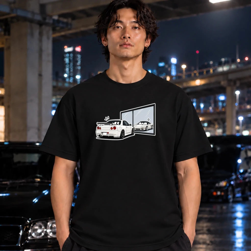 A man wearing a black t-shirt with a white and gray car graphic print, standing in a wet urban street at night with blurred cars and city lights in the background.