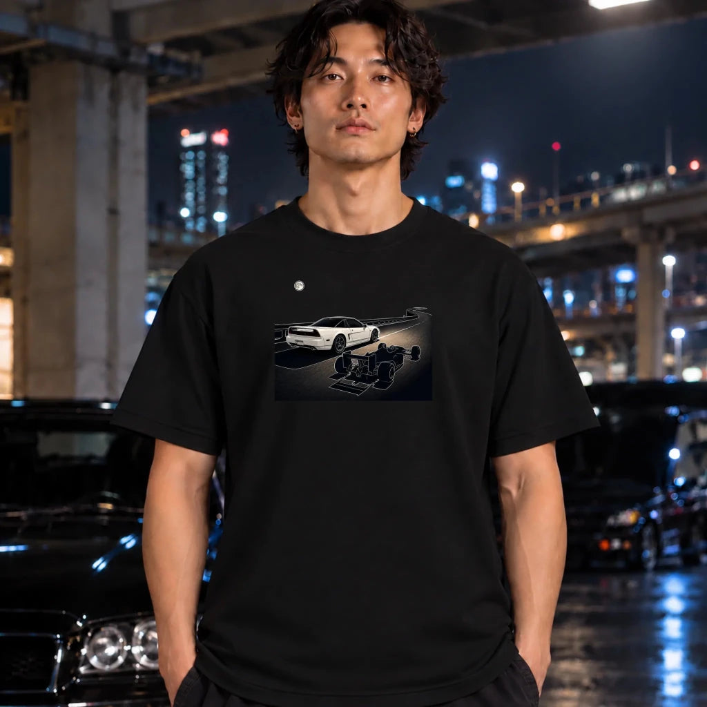 A man wearing a black t-shirt with a graphic print of a white sports car and a drag racer, standing in a nighttime urban setting with blurred cars and city lights in the background.