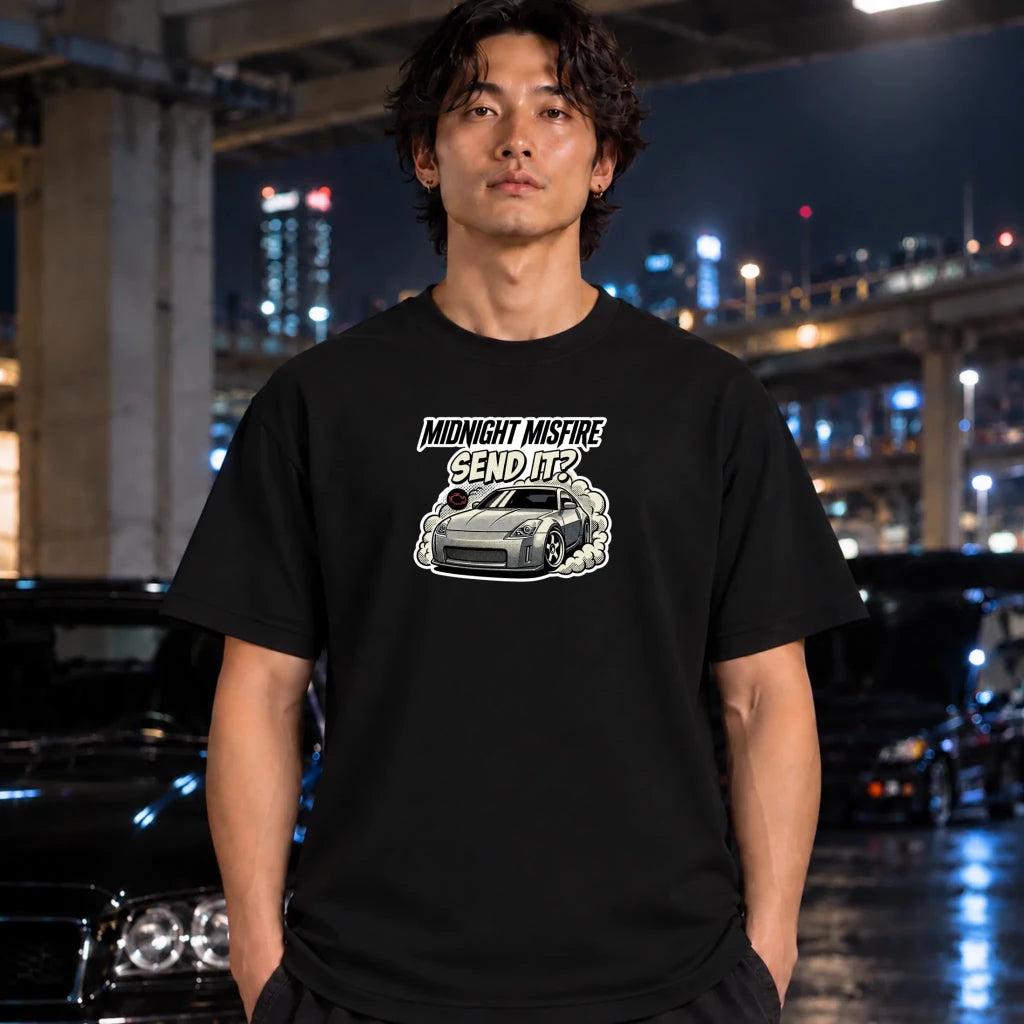  man wearing a black short-sleeve t-shirt with a graphic print of a silver sports car and the text 'MIDNIGHT MISFIRE SEND IT?' on the chest,