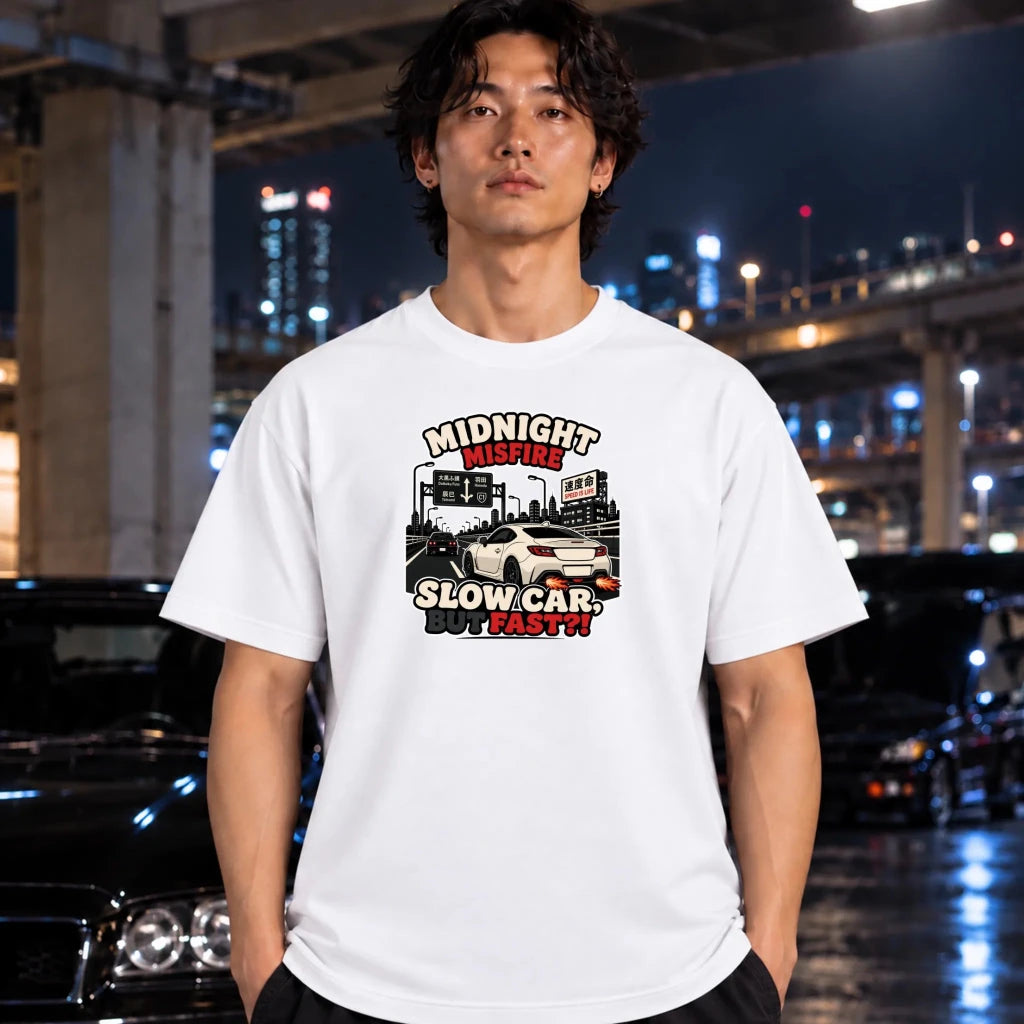 A man wearing a white graphic t-shirt with a 'Midnight Misfire - Slow Car, but fast!' print, standing in a wet, nighttime urban environment with cars and city lights in the background.
