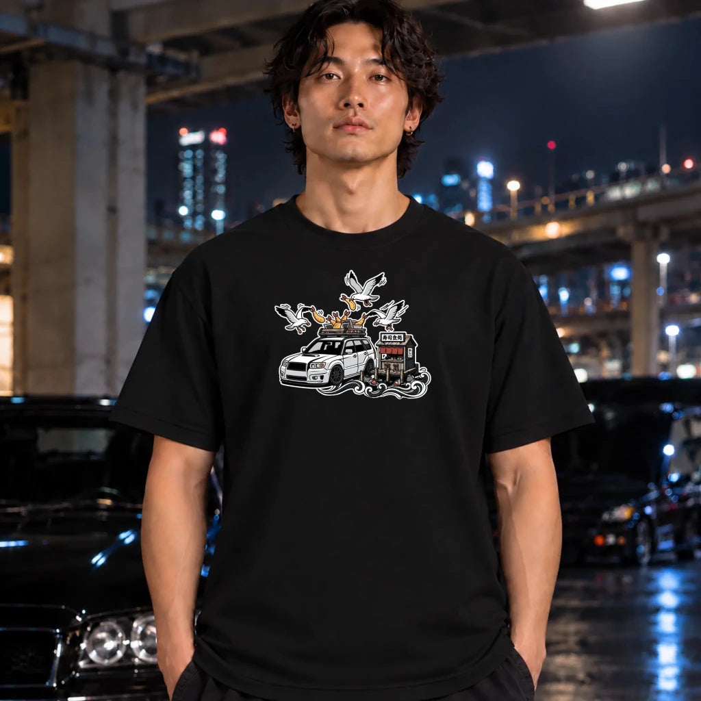man wearing a black crewneck t-shirt with a graphic print of a white station wagon with a roof rack, surrounded by seagulls and a small building.