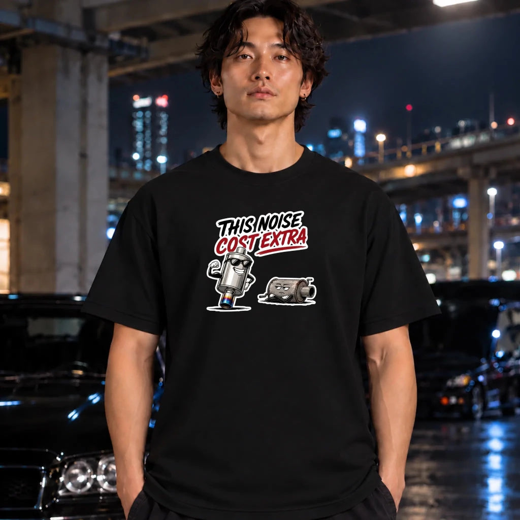  man wearing a black short-sleeve t-shirt. The shirt features a graphic print of a cartoon character with the text 'THIS NOISE COST EXTRA' in white and red.