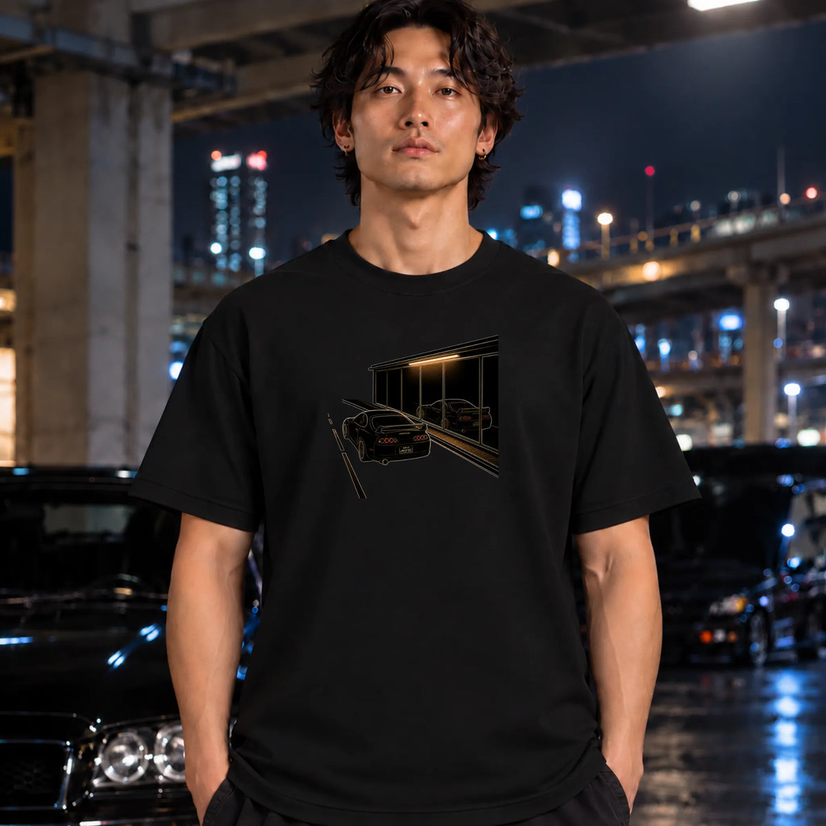 A black short-sleeve t-shirt worn by a man, featuring a graphic print of a black sports car in front of a dark building with warm light. 