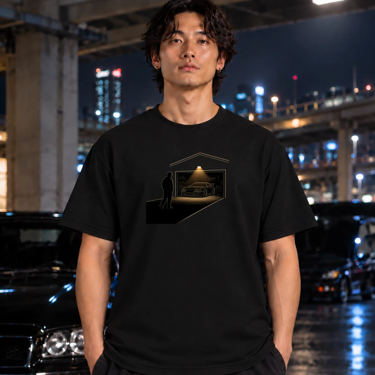 man wearing black t-shirt featuring a graphic print of a silhouette of a man looking at a sports car inside a garage.