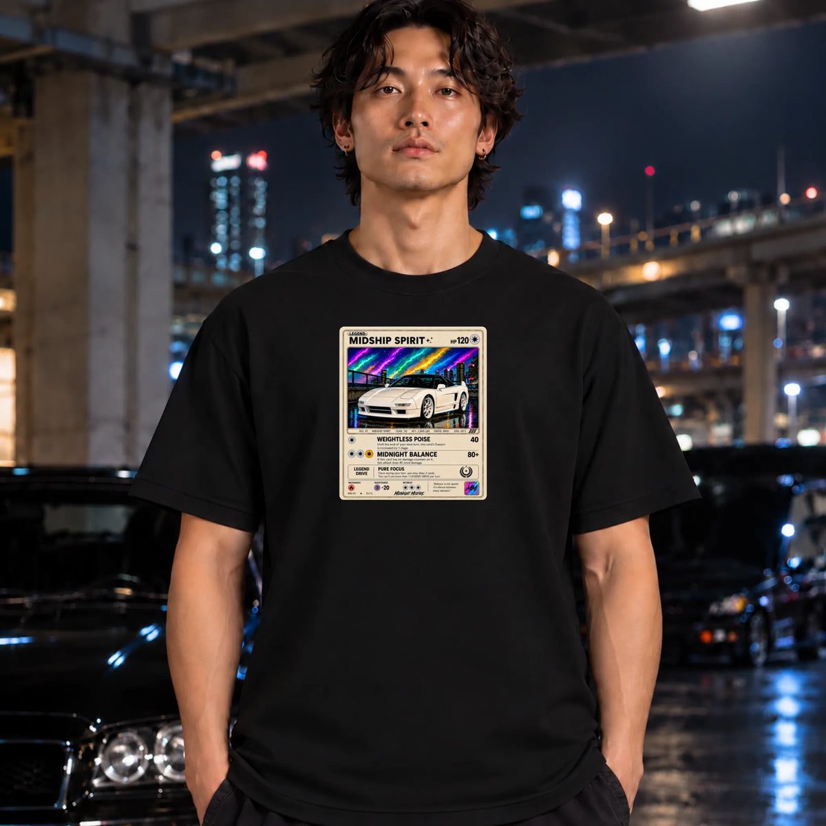A man wearing a black t-shirt with a Pokémon-style graphic print featuring a white sports car and rainbow accents, standing in a city environment at night.