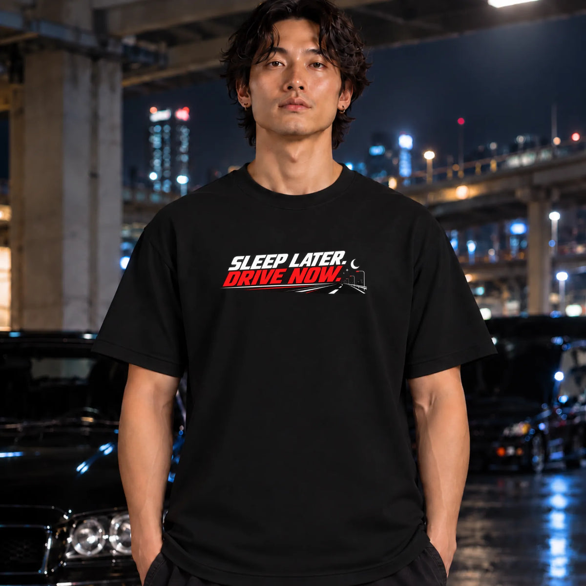 A man wearing a black graphic t-shirt with the text 'SLEEP LATER. DRIVE NOW.