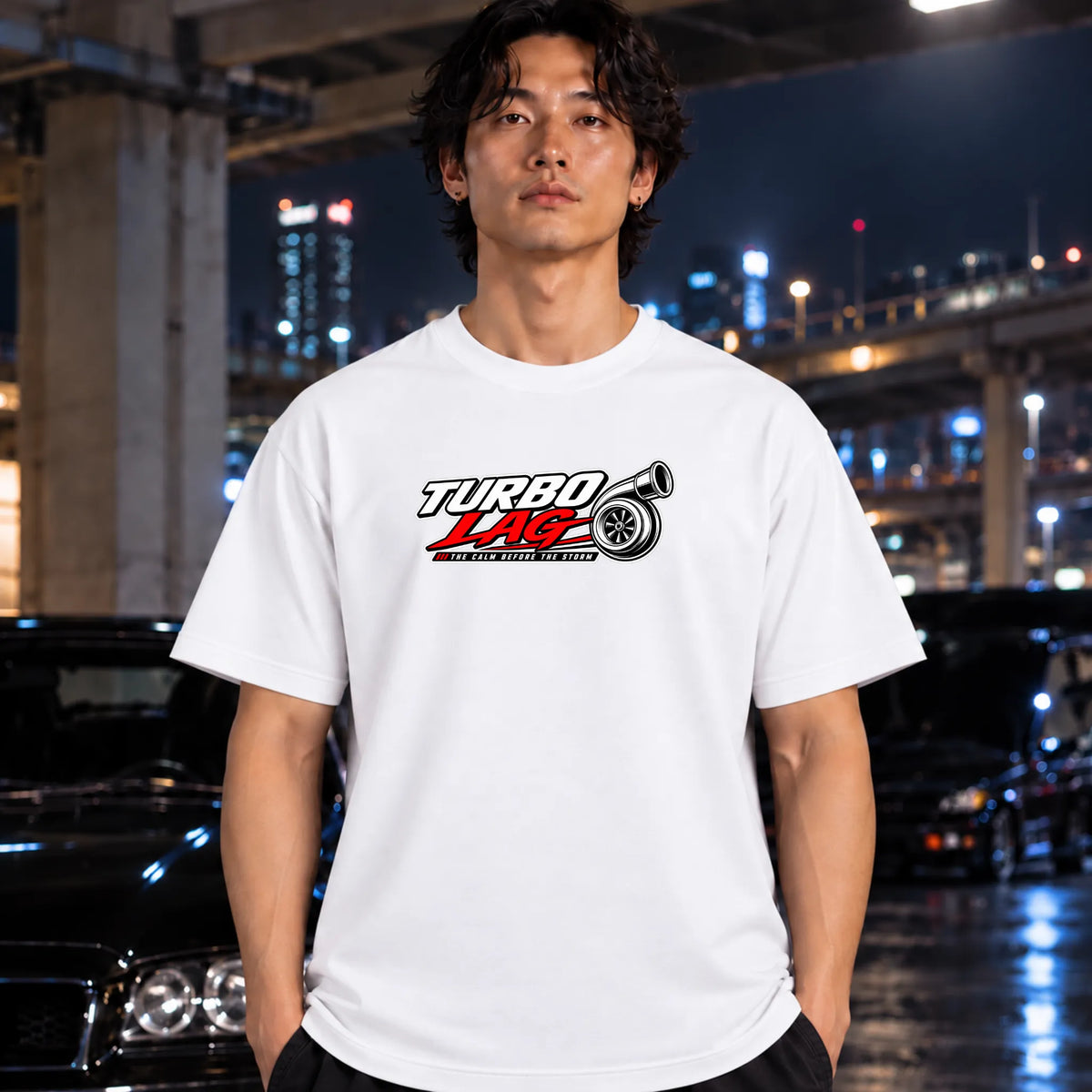 A man wearing a white short-sleeve t-shirt with a 'Turbo Lab' graphic on the chest, standing in front of a blurred night cityscape with cars.
