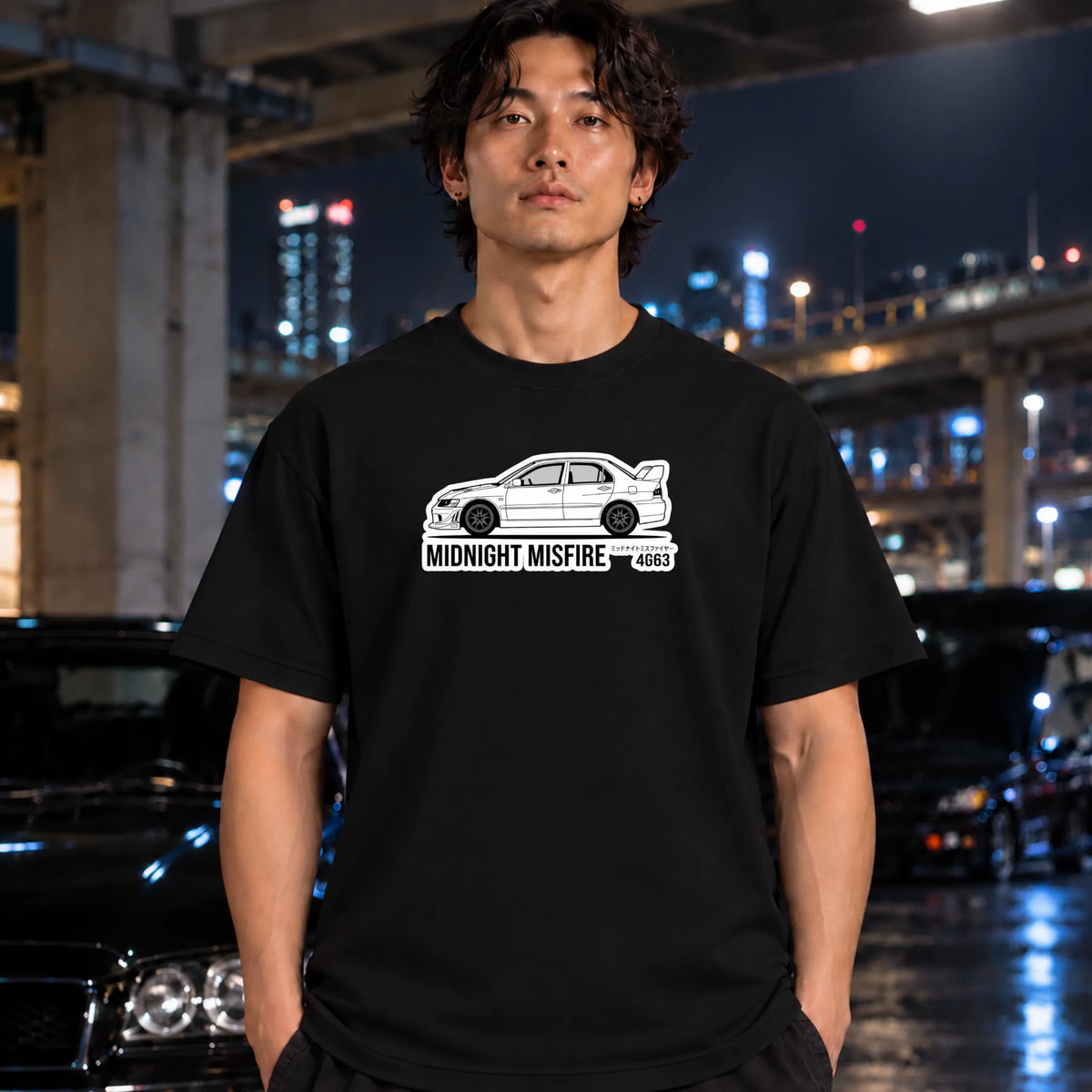 A man wearing a black t-shirt with a white graphic of a car and the text 'MIDNIGHT MISFIRE 4G63' stands in front of a blurred night city background with cars.