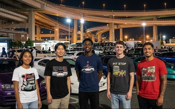 Group of people standing in front of cars at a car meet event with a complex highway in the background.