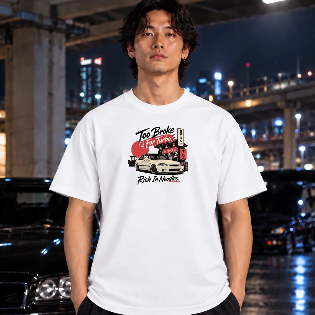 A man wearing a white graphic t-shirt with a 'Too Broke to Care Turbo' car illustration, standing in a wet city street at night with cars and bridge lights in the background.